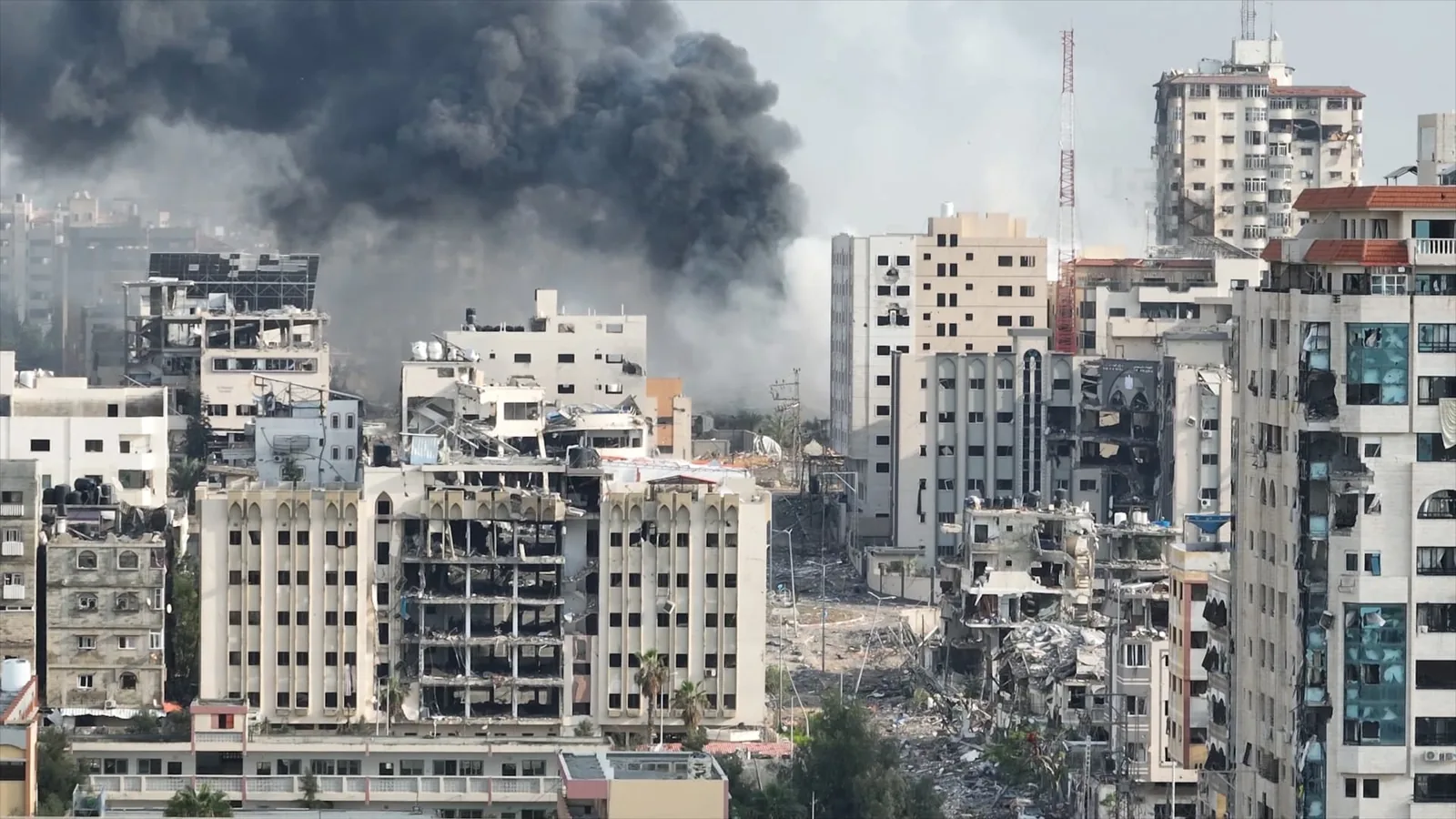 A wide city view shows damaged buildings and a dark smoke plume in the distance.