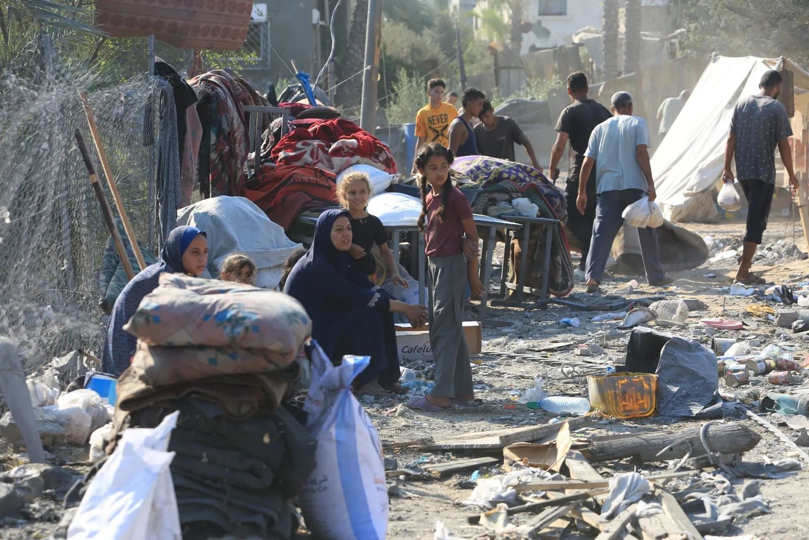 A group of people move belongings through a damaged neighborhood.